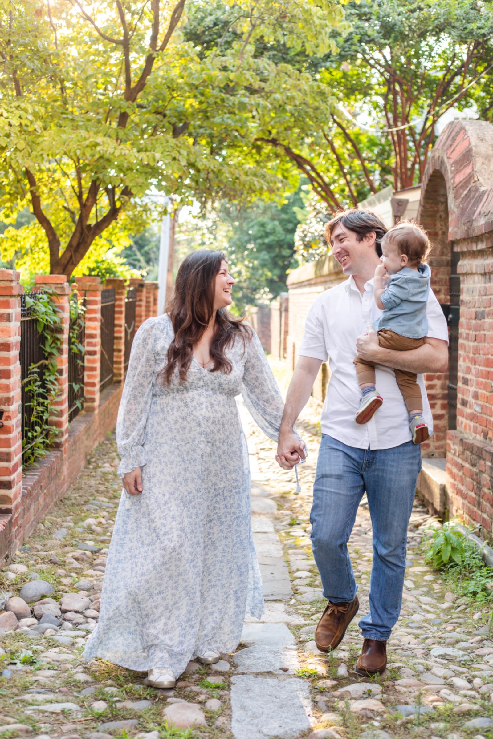 Parents holding hands walking a cobblestone alley with their toddler son