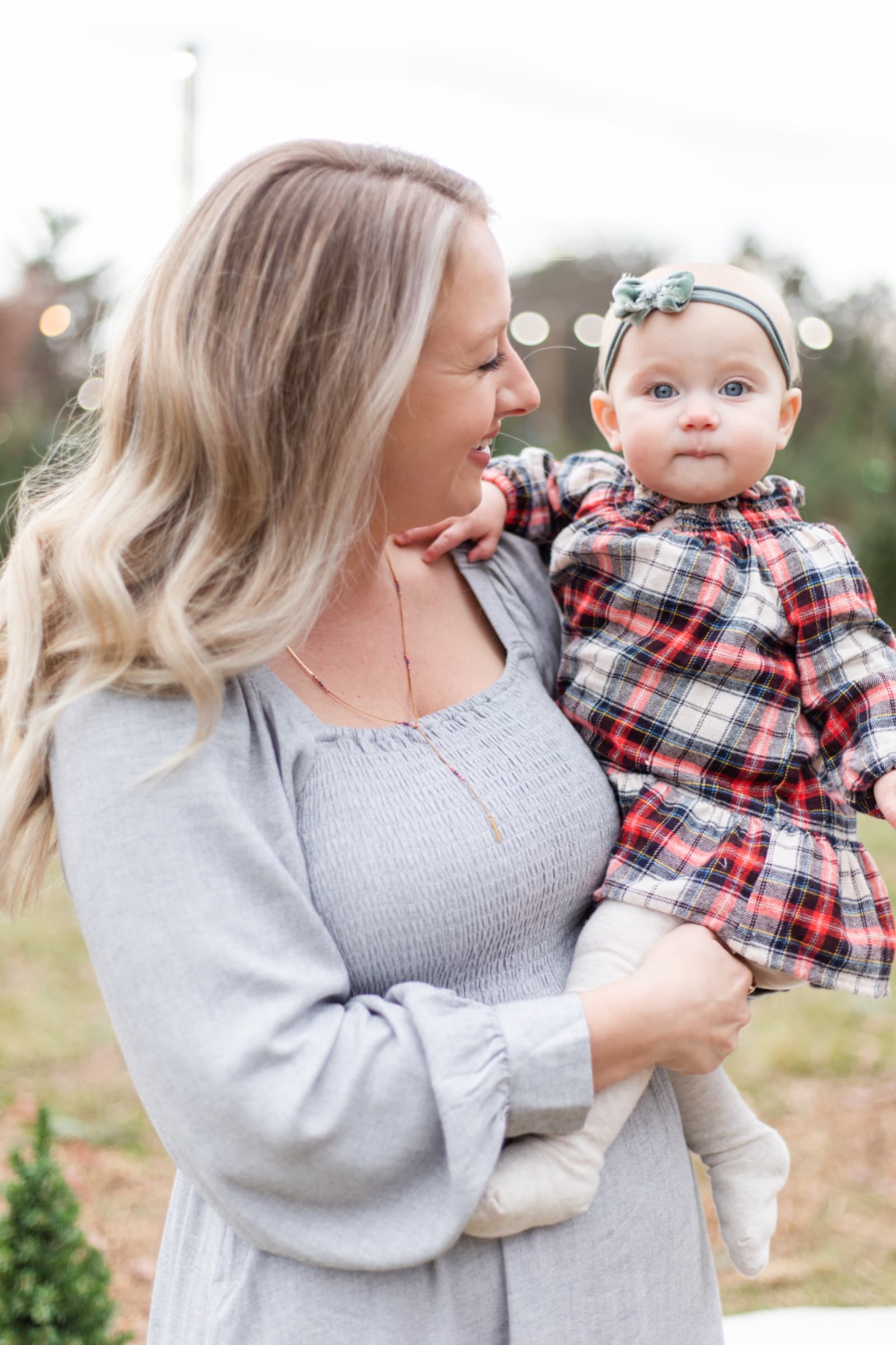 Mother holding her baby girl in plaid at a tree farm