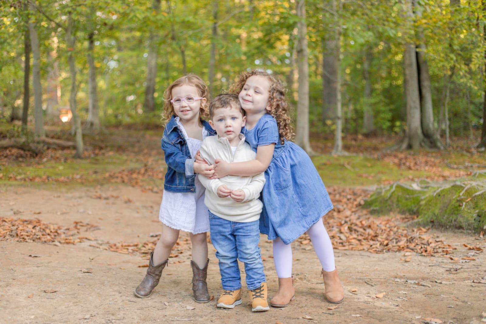 Three young siblings hugging on a woodland path