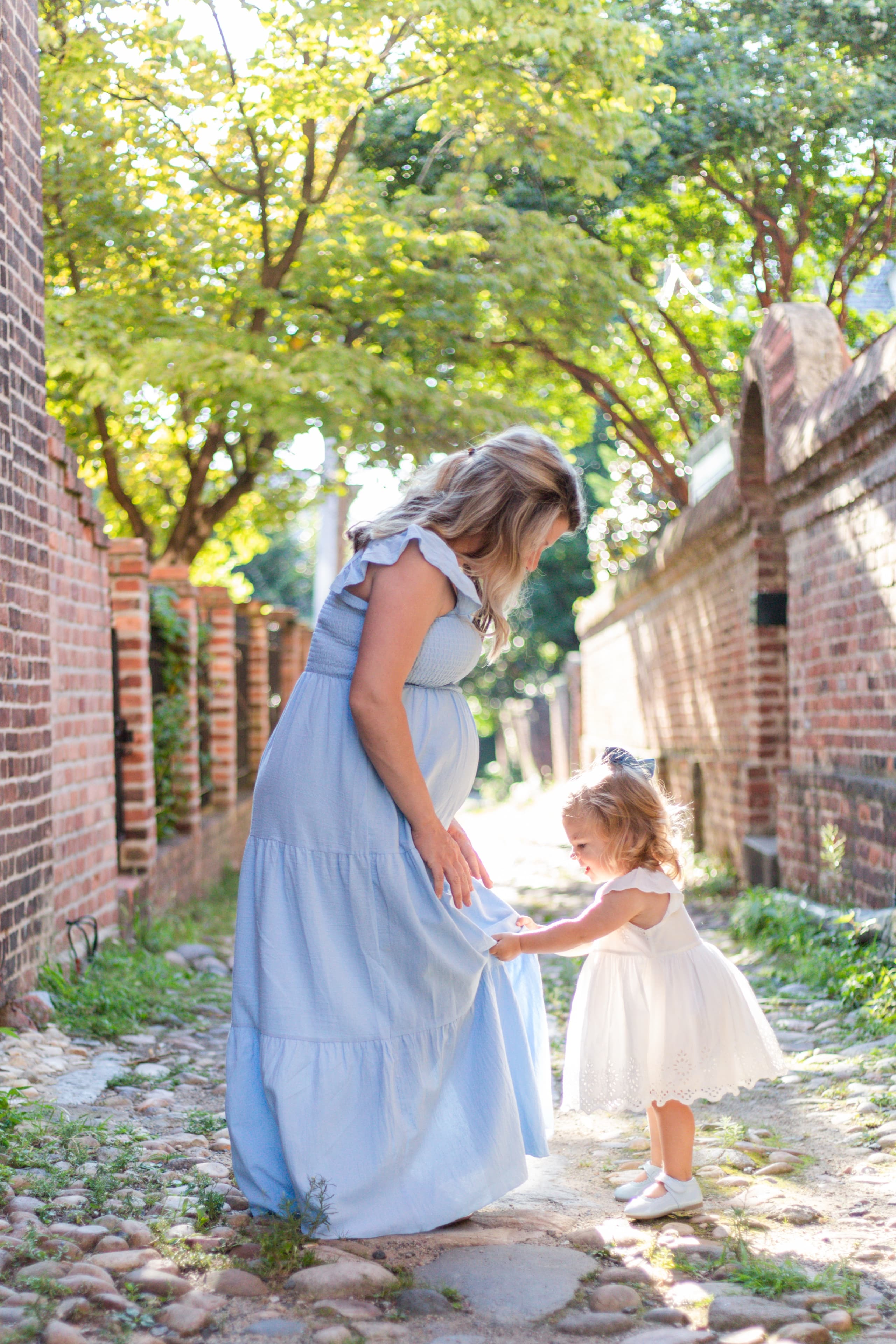 Expecting mother in blue with her toddler daughter in a cobblestone alley