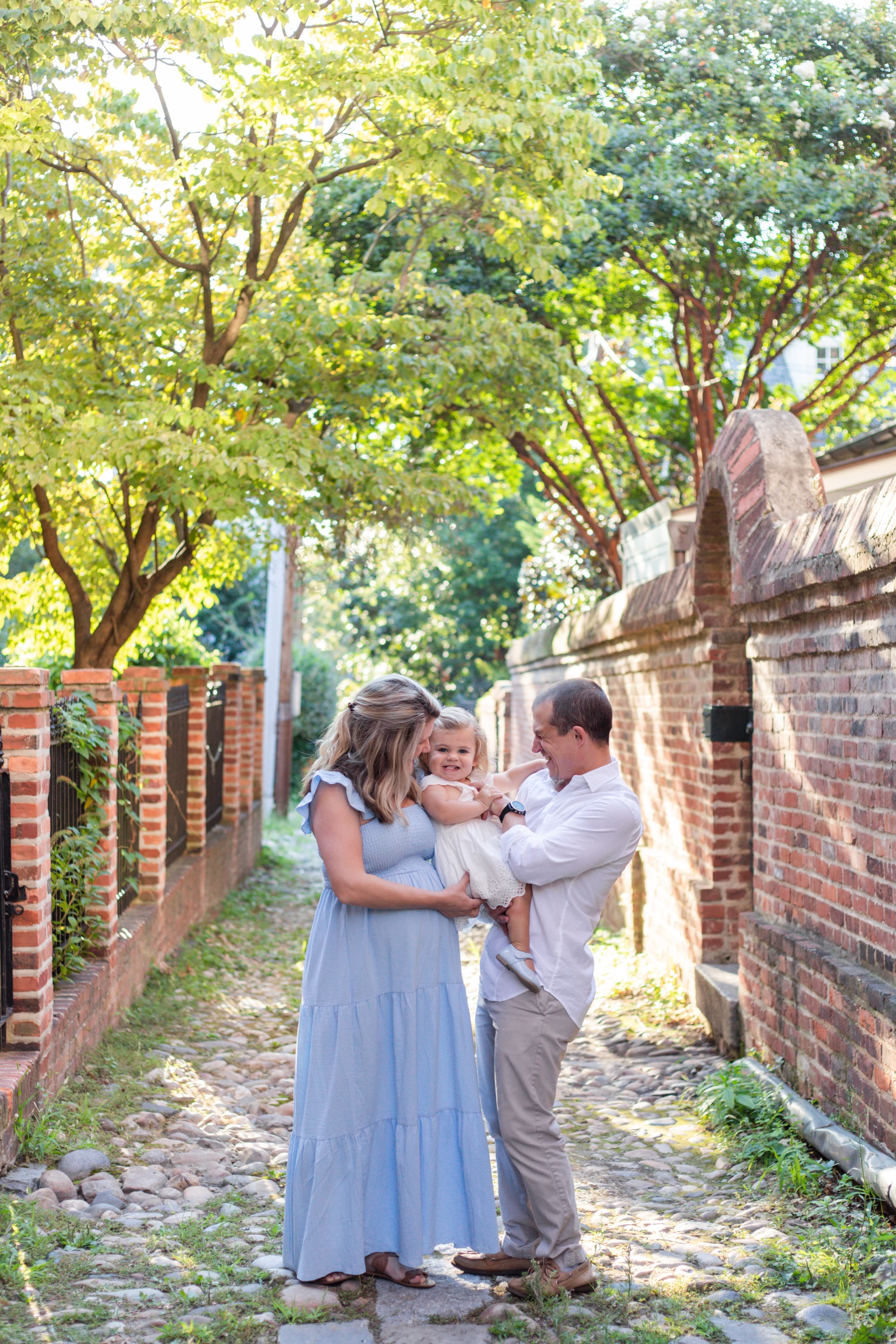Expecting parents holding their toddler daughter, all laughing