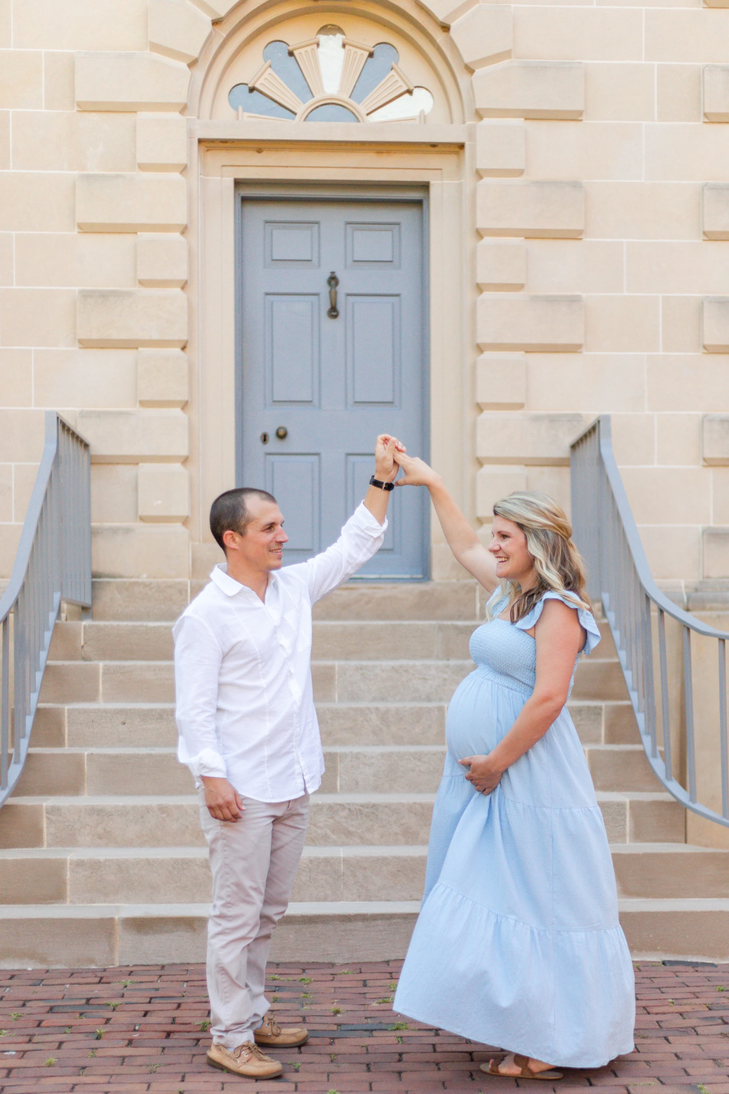 Expecting couple dancing in front of a blue door