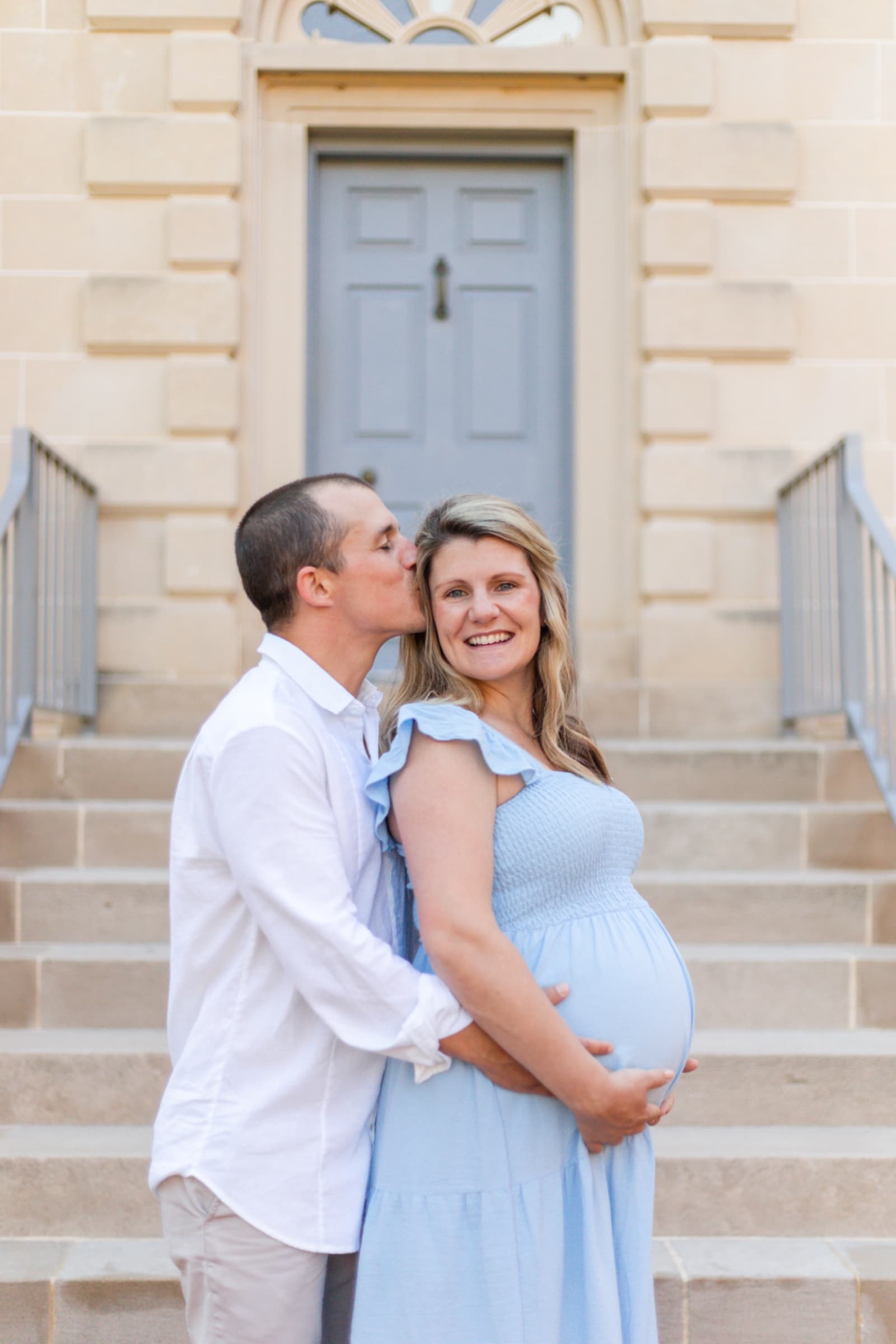 Expecting couple embracing on stone steps, husband kissing her temple