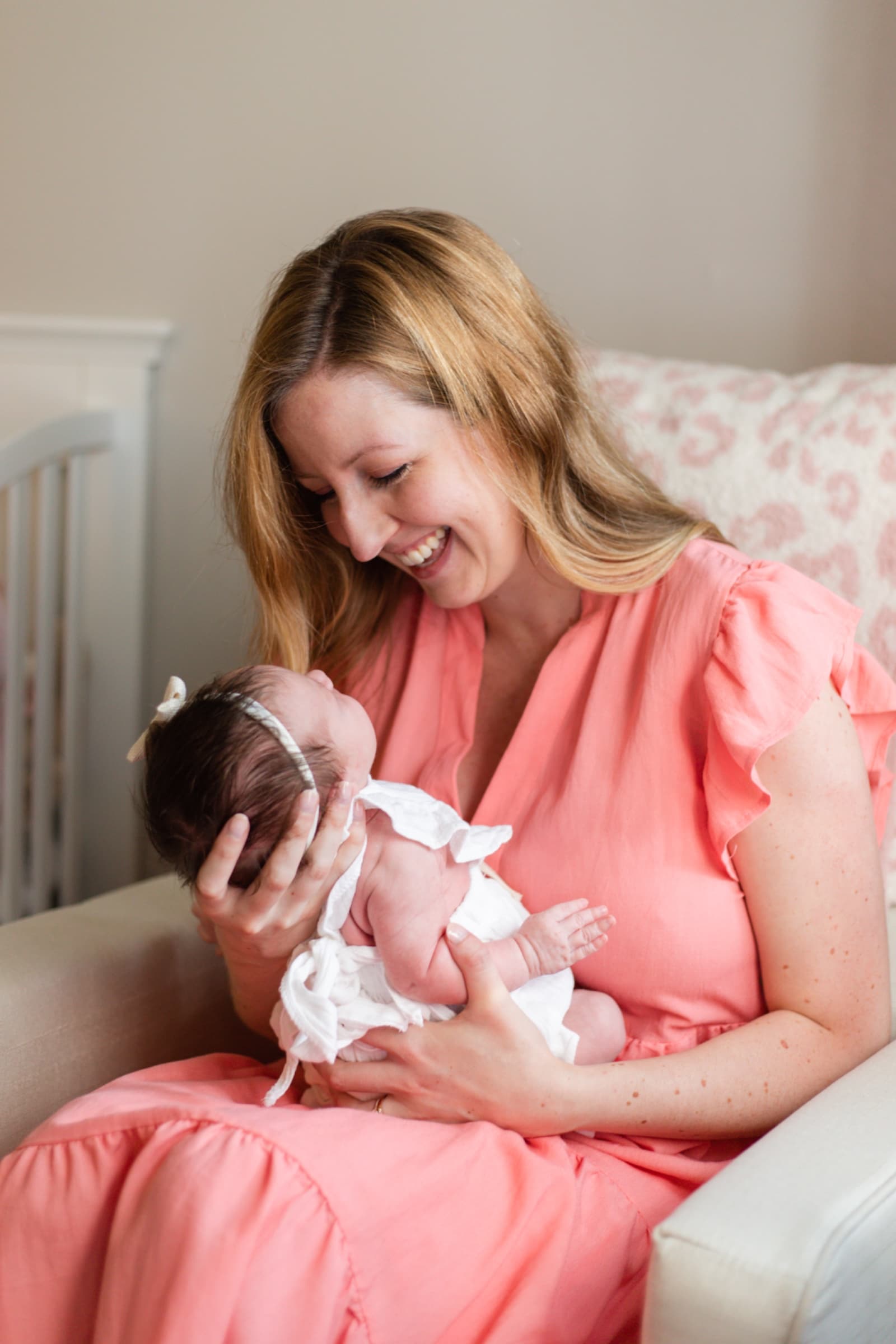 Mother in coral cradling her newborn, laughing